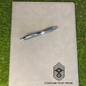 May include: A light gray rectangular portfolio folder with a smooth, leather-like texture. The bottom right corner features a black engraved military rank insignia of a chevron with a star, followed by the black text Custom Text Here.