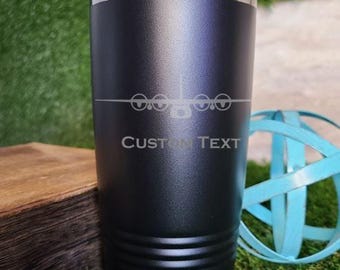 May include: A matte black stainless steel tumbler with a clear lid, featuring a laser-engraved graphic of a four-engine aircraft silhouette above the text CUSTOM TEXT. The cylindrical vessel has a textured finish and horizontal ridges at the base.