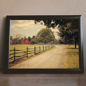 May include: A framed photograph of a red barn in a rural setting. The barn is surrounded by a wooden fence and a dirt road leads away from it. The photo has a vintage, faded look.