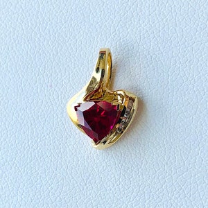 May include: A gold pendant with a red heart-shaped gemstone and small clear gemstones around the edge.