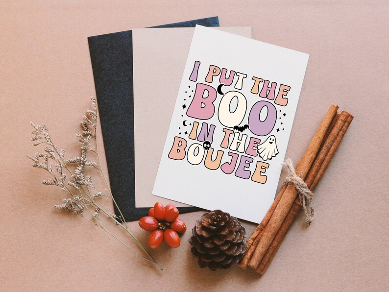 Puede incluir: Una tarjeta blanca con el texto "I put the BOO in the BOUJEE" en letras de colores. La tarjeta est&aacute; rodeada de un fondo marr&oacute;n con palitos de canela y una pi&ntilde;a.