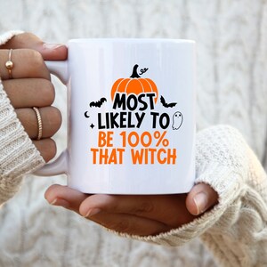 May include: White ceramic mug with a black and orange design. The mug features a pumpkin, bats, and the text "Most Likely to Be 100% That Witch".
