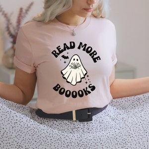 May include: A pink t-shirt with a ghost holding a book and the text "Read More Booooks".
