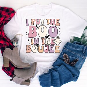Puede incluir: Una camiseta blanca con el texto "I put the BOO in the BOUJEE" en una fuente retro con colores pastel y gr&aacute;ficos de Halloween.