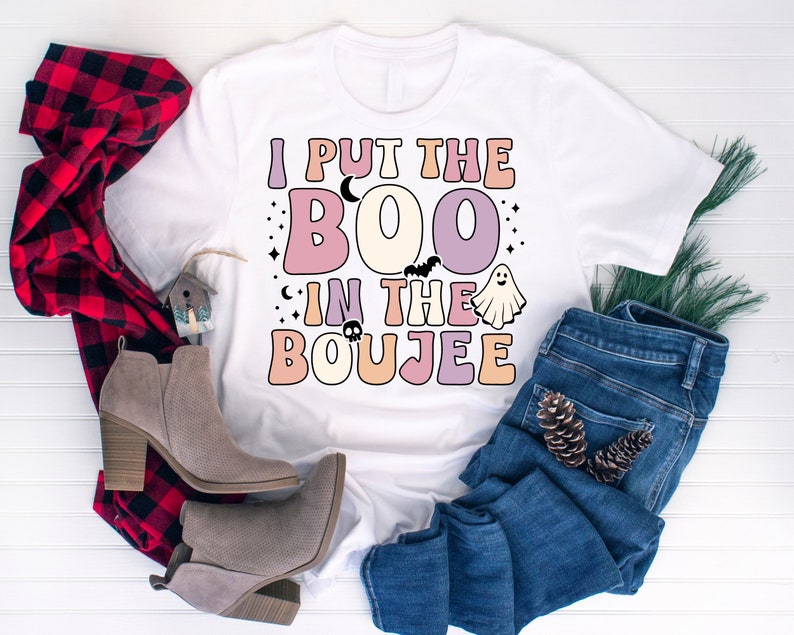 Puede incluir: Una camiseta blanca con el texto "I put the BOO in the BOUJEE" en una fuente retro con colores pastel y gr&aacute;ficos de Halloween.