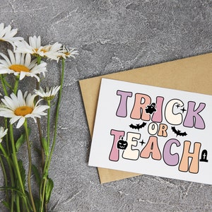 May include: A white card with the text "Trick or Teach" in pink, purple, and orange letters. The text is decorated with a ghost, bats, a pumpkin, and a tombstone. The card is on a brown envelope.