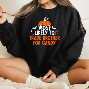 May include: Black sweatshirt with a Halloween-themed graphic that says "Most Likely to Trade Brother for Candy". The graphic features a pumpkin, bats, and a ghost.