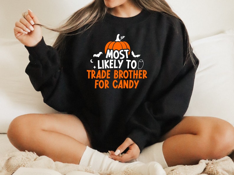 May include: Black sweatshirt with a Halloween-themed graphic that says "Most Likely to Trade Brother for Candy". The graphic features a pumpkin, bats, and a ghost.