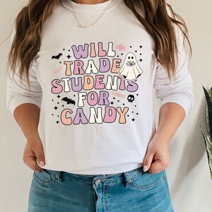 May include: White long-sleeved sweatshirt with a pink, purple, and orange graphic that says "Will Trade Students For Candy" with a ghost and bats.