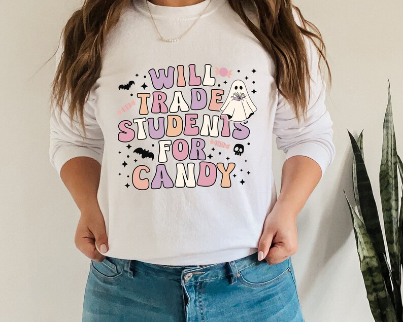 May include: White long-sleeved sweatshirt with a pink, purple, and orange graphic that says "Will Trade Students For Candy" with a ghost and bats.