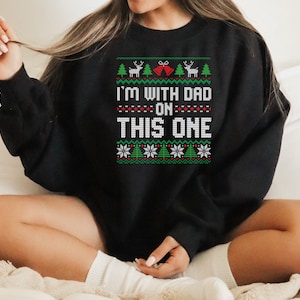 May include: Black Christmas sweater with a white and green knit pattern. The sweater has the text "I'm with Dad on this one" in white.