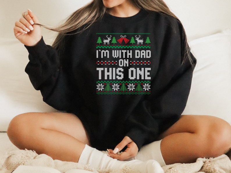 May include: Black Christmas sweater with a white and green knit pattern. The sweater has the text "I'm with Dad on this one" in white.