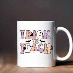 May include: White ceramic coffee mug with a pink, orange, and purple design that says "Trick or Teach" with a ghost, bat, pumpkin, and tombstone graphic.