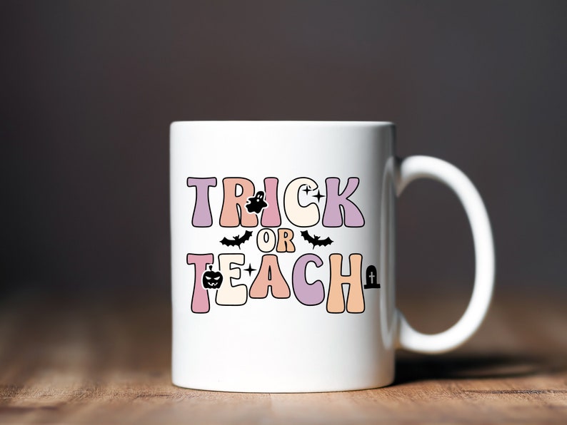May include: White ceramic coffee mug with a pink, orange, and purple design that says "Trick or Teach" with a ghost, bat, pumpkin, and tombstone graphic.