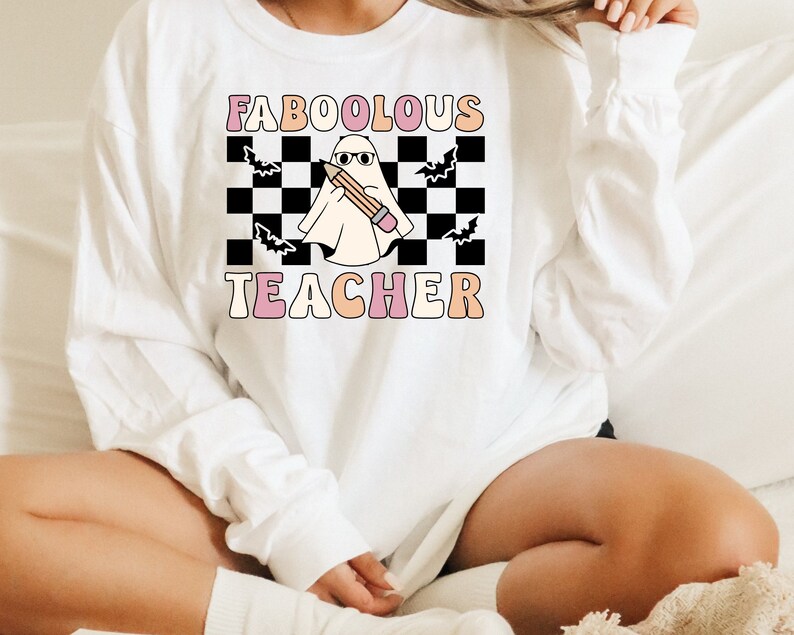May include: White sweatshirt with a black and white checkered background, a ghost holding a pencil, and the text "FABOOLOUS TEACHER" in pink and orange letters.