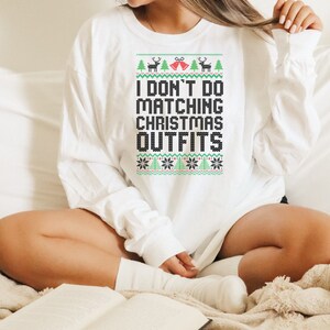 May include: White long-sleeve sweatshirt with a festive Christmas-themed design. The text on the sweatshirt reads "I don't do matching Christmas outfits".