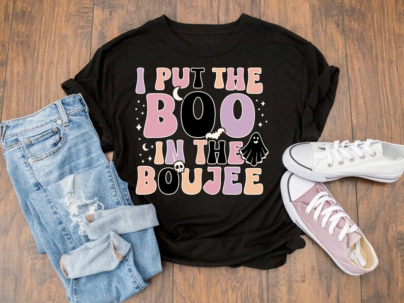 Puede incluir: Camiseta negra con un estampado gr&aacute;fico que dice "I put the boo in the boujee" en letras rosa, morado y naranja. El gr&aacute;fico tambi&eacute;n incluye un fantasma, un murci&eacute;lago y una calavera.