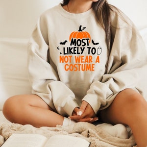May include: A light beige sweatshirt with a pumpkin graphic and the text "Most Likely To Not Wear A Costume".