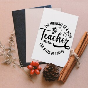 May include: A white card with black text that reads "The influence of a good teacher can never be erased". The text is in a circle with a globe, apple, pencil, and hearts around it. The card is on a brown surface with cinnamon sticks, a pine cone, and red berries.