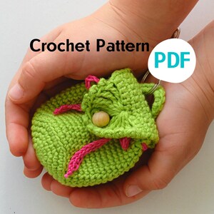 Puede incluir: Una bolsa de crochet verde con ribete rosa y un botón de madera. La bolsa está siendo sostenida en las manos de una persona. El texto "Crochet Pattern PDF" es visible en la imagen.