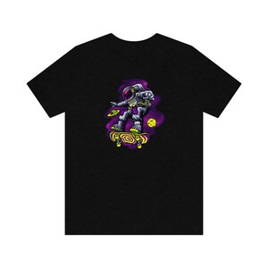 May include: Black t-shirt with a graphic of an astronaut skateboarding in space. The astronaut is wearing a white spacesuit with a purple helmet and is holding a skateboard with yellow wheels. The background is a purple and black galaxy with stars and planets.