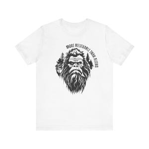 May include: White t-shirt with a black and white illustration of Bigfoot in a forest setting. The text "More believable than aliens" is printed in a circle around Bigfoot.