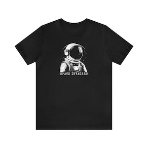 May include: Black t-shirt with a white illustration of an astronaut wearing a helmet and the text "SPACE INVADERS" underneath.