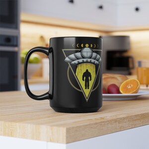 May include: Black coffee mug with a graphic of a Bigfoot standing in front of a UFO. The UFO is in a triangle with a yellow outline and the words "C.O.D." above it.