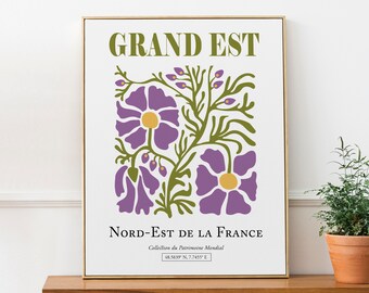 May include: A white poster with a green and purple floral design. The text "GRAND EST" is at the top of the poster. The text "NORD-EST DE LA FRANCE" is at the bottom of the poster. The text "Collection du Patrimoine Mondial" is below the text "NORD-EST DE LA FRANCE". The text "48.5839 N. 7.7455" E is at the bottom of the poster.