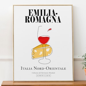 Op de afbeelding: Een minimalistische lijnillustratie van een glas rode wijn en een stuk kaas, met de tekst "EMILIA-ROMAGNA" in zwart boven de afbeelding en "ITALIA NORD-ORIENTALE" in zwart onder de afbeelding. De tekst "Collezione del Patrimonio Mondiale" staat in kleinere zwarte tekst onder de hoofdtekst, en de coördinaten "44.5968" N 11.2186" E" staan in nog kleinere zwarte tekst onder de vorige tekst.