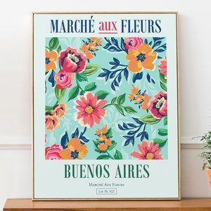 Può includere: Un poster incorniciato con un motivo floreale in tonalità rosa, arancio, giallo e verde su uno sfondo blu chiaro. Il testo "MARCHÉ aux FLEURS" è in alto e "BUENOS AIRES" in basso. Il testo "MARCHÉ aux FLEURS Lot No. 022" è in un carattere più piccolo sotto il nome della città.