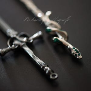 Peut inclure: Deux colliers en argent, l'un avec un pendentif en forme d'épée et l'autre avec un pendentif en forme de serpent. Le pendentif en forme de serpent est orné de pierres précieuses vertes.