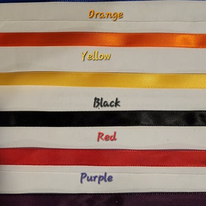 May include: A selection of colorful ribbons in pink, green, blue, orange, yellow, black, red, purple, white, and gold. Each ribbon is displayed horizontally with the color name written above it.