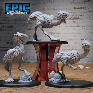May include: Three grey painted miniature figurines of a mythical bird with feathery plumage and a long neck. The figurines are posed on circular bases with a textured egg design.