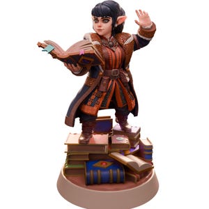 May include: A small, dark-haired elf figurine wearing a blue and orange robe, holding a book open, standing on a stack of books. The figurine is painted in a realistic style and has a whimsical expression.