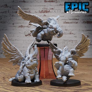 Puede incluir: Tres figuras de elefantes en miniatura grises con grandes alas emplumadas. Una está en pleno vuelo, otra está sentada y la tercera está de pie. Las figuras están sobre bases negras, con el texto "EPIC Miniatures" en la esquina superior derecha.