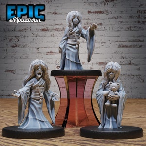 May include: Three painted figurines of ghostly figures in white robes. The figures are posed in different positions, one with arms outstretched, one with arms raised, and one holding a teddy bear. The figures are on black bases.