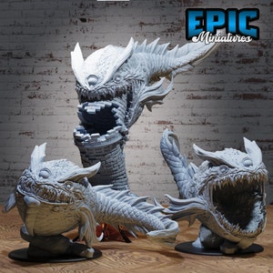 May include: Three gray, detailed, 3D printed fantasy creature miniatures. The creatures are a dragon, a fish-like creature, and a creature with a large mouth. The miniatures are on a wooden surface.