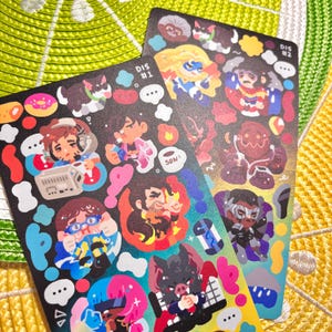 May include: Two sticker sheets with colorful cartoon illustrations. One sheet is labeled "DIS #1" and the other "DIS #2". The stickers feature various characters, speech bubbles, and other graphic elements in a variety of colors, including pink, blue, and red.