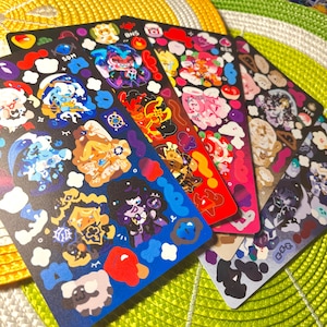 May include: A collection of colorful sticker sheets featuring various cartoon characters and designs. The stickers are arranged on a yellow and green textured surface. Each sheet has a unique color scheme, including blue, red, and purple.