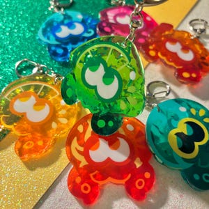 Peut inclure: Plusieurs porte-clés en acrylique colorés, dans des tons de bleu, vert, orange et rouge. Chaque porte-clés présente un design unique avec un chiffre trois blanc et un porte-clés argenté.
