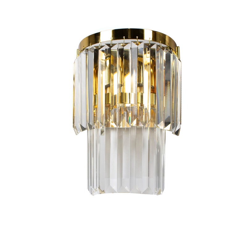 May include: A gold-toned wall sconce with a crystal chandelier design. The sconce has two tiers of crystal prisms that hang from a circular base.