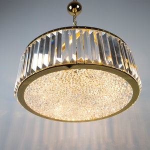 Pu&ograve; includere: Un lampadario dorato con un design rotondo in cristallo. Il lampadario ha una fonte di luce centrale circondata da un anello di prismi di cristallo.