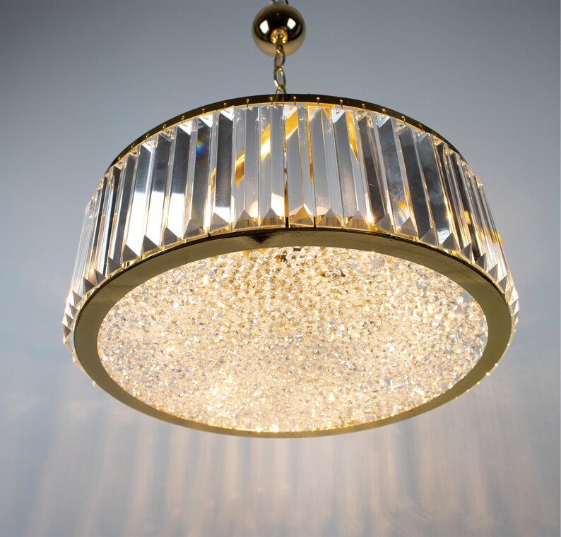 Pu&ograve; includere: Un lampadario dorato con un design rotondo in cristallo. Il lampadario ha una fonte di luce centrale circondata da un anello di prismi di cristallo.