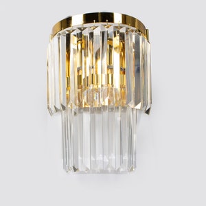 May include: A gold wall sconce with clear crystal prisms. The sconce has a circular base and two tiers of prisms.