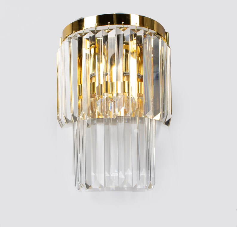 May include: A gold wall sconce with clear crystal prisms. The sconce has a circular base and two tiers of prisms.