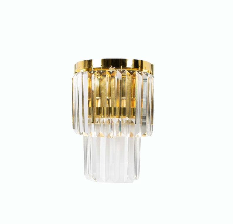 May include: A gold and crystal wall sconce with a geometric design. The sconce has two tiers of crystal prisms.