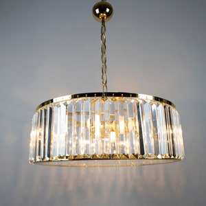 Pu&ograve; includere: Un lampadario dorato con prismi di cristallo trasparente appesi a una catena dorata. Il lampadario ha una forma rotonda ed &egrave; illuminato da pi&ugrave; lampadine.