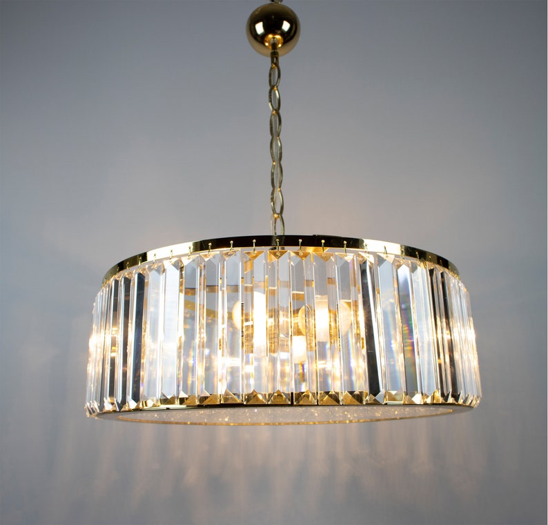 Pu&ograve; includere: Un lampadario dorato con prismi di cristallo trasparente appesi a una catena dorata. Il lampadario ha una forma rotonda ed &egrave; illuminato da pi&ugrave; lampadine.