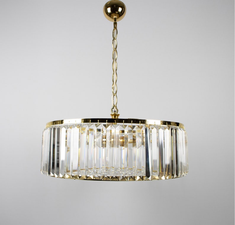 Pu&ograve; includere: Un lampadario rotondo in cristallo con finitura dorata. Il lampadario &egrave; appeso al soffitto da una catena.